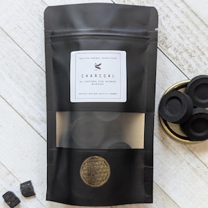 Puede incluir: Una bolsa negra resellable que contiene discos de carbón para quemar incienso. La etiqueta dice "SEKHEM HERBAL TRADITIONS CHARCOAL ALL NATURAL FOR INCENSE BURNING SACRED ANCIENT QUALITY HERBS" con un símbolo dorado de la flor de la vida.