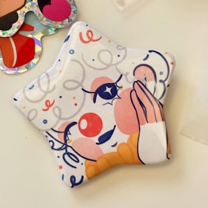 Può includere: Un adesivo a forma di stella con un fantasioso design a forma di faccia da clown. L'adesivo presenta uno sfondo bianco con un volto da clown dei cartoni animati, tra cui un naso rosso, guance rosa e occhi blu. Il design include coriandoli e linee ricci.