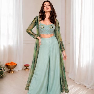 May include: A three-piece outfit comprising a light blue crop top and wide-leg trousers. A sheer, long-sleeved green jacket with a floral pattern completes the ensemble. Suitable for a special occasion.