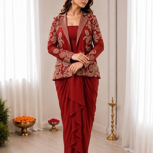 May include: A deep red ensemble consisting of a long-sleeved blazer and a matching floor-length skirt. The blazer features intricate gold embroidery on the lapels, sleeves, and front panels. The skirt has a draped, ruffled front design.