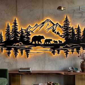 Pode incluir: Uma peça de arte de parede em metal preto com a silhueta de uma cordilheira, uma floresta de pinheiros e uma família de ursos a caminhar, iluminada por trás por uma luz dourada quente que projeta um reflexo na superfície da parede.