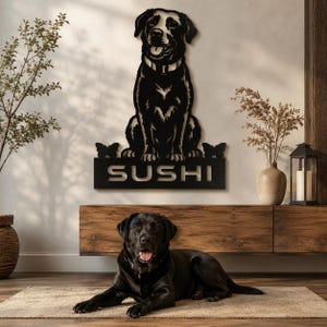 May include: A black metal wall art piece featuring a sitting Labrador retriever with a collar, flanked by two small butterfly silhouettes, mounted above a rectangular nameplate with the cutout text SUSHI in a bold, sans-serif typeface.