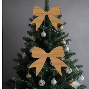 Op de afbeelding: Een versierde kerstboom met houten strikversieringen en zilveren ballen. De boom is bekroond met een gouden ster. De lichtbruine houten strikken geven de decoratie een rustieke uitstraling.