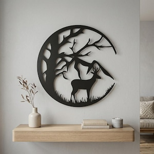 May include: A circular black metal wall art piece featuring a silhouette of a deer standing in grass beneath a large tree and mountain range. The design is open-cut, creating a detailed nature scene within the circular frame.