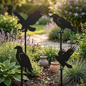 Op de afbeelding: Zwarte metalen tuindecoratie met vier vogel silhouetten: twee adelaars en twee raven. De vogels zijn op palen gemonteerd, perfect voor buiten. De adelaars zijn in vlucht, terwijl de raven zitten. De tekst "ARTISAN BLACK METAL GARDEN DECOR" is zichtbaar.
