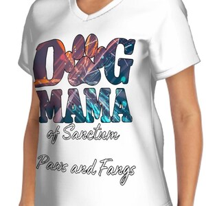 May include: White v-neck t-shirt with the text "DOG MAMA" in a colorful, paw-print design. Below the text are the words "of Sanctum" and "Paws and Fangs" in a script font. The shirt is made of a soft material.