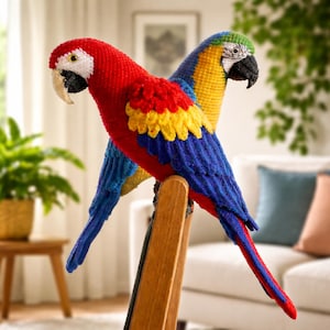 以下が含まれることがあります： 木製の椅子に止まっている、赤と青と黄色の手作りの編み物オウムが2羽います。赤いオウムは白い顔と黒い嘴があり、青と黄色のオウムは緑色の頭をしています。オウムは鮮やかな色で詳細に表現されています。