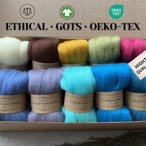 Puede incluir: Una caja de lana merino de colores blanco, marrón, amarillo, verde, rosa y azul. La caja está etiquetada como "ETHICAL • GOTS • OEKO-TEX" y tiene una etiqueta de "HIGH QUALITY". Cada ovillo de lana está envuelto con una etiqueta de papel.