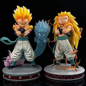 Puede incluir: Dos figuras de acción de personajes de anime con pelo amarillo puntiagudo y pantalones blancos. Una figura tiene el pelo corto y los brazos cruzados, la otra tiene el pelo largo. Una figura azul fantasmal se encuentra entre ellas. Las figuras están sobre bases redondas.