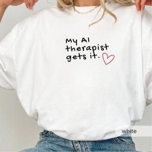 Op de afbeelding: Wit T-shirt met de zwarte tekst "My AI therapist gets it." en een rood hart. Het shirt heeft een casual stijl en is geschikt voor dagelijks gebruik.