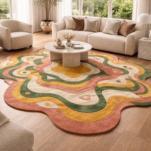 May include: A colorful, abstract area rug with a wavy design in shades of pink, yellow, green, and cream. The rug is placed on a hardwood floor in a living room setting, with a sofa and armchair visible.
