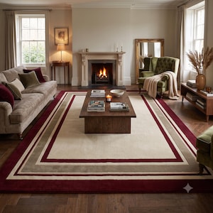May include: A large rectangular area rug featuring a central cream-colored field framed by concentric borders in shades of taupe, white, and deep burgundy. The rug has a smooth, low-pile texture and covers a significant portion of the wooden floor.