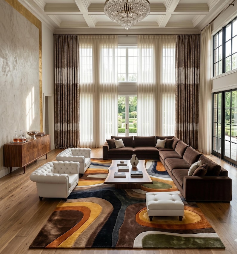 May include: A luxurious living room featuring a large brown sectional sofa, two white tufted armchairs, and a patterned area rug with shades of brown, yellow, and blue. The room has tall windows with sheer curtains and a crystal chandelier.