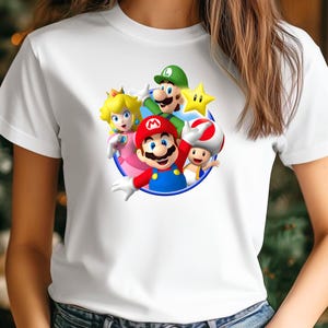 Op de afbeelding: Wit T-shirt met een kleurrijke afbeelding van Mario, Luigi, Princess Peach, Toad en een ster. De personages staan in een cirkel met een blauwe rand. Het shirt is gemaakt van een zacht, wit materiaal.