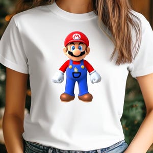 Op de afbeelding: Wit T-shirt met een afbeelding van het videogamepersonage Mario. Mario wordt getoond met zijn rode hoed, blauwe overall en bruine schoenen. Het T-shirt heeft een ronde hals.