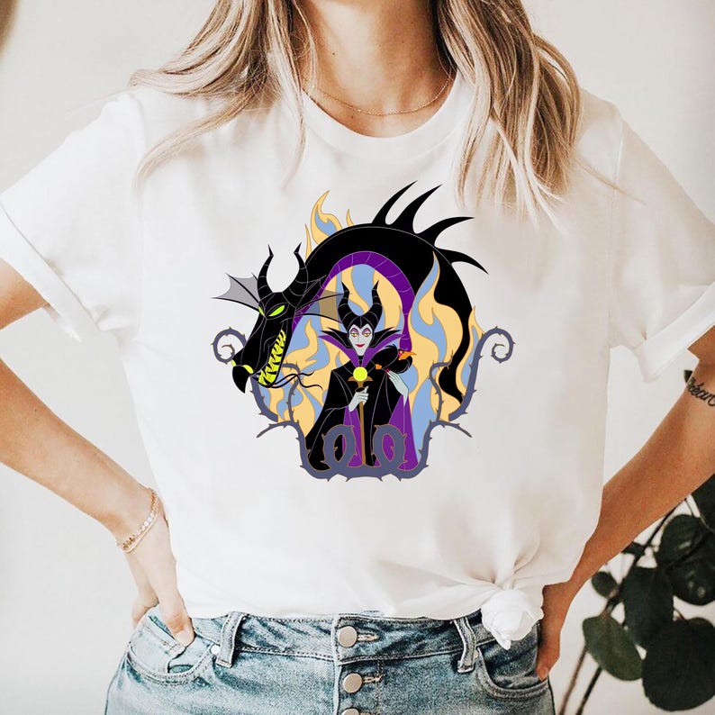 May include: White t-shirt featuring a cartoon graphic of a dragon and a character with a black and purple outfit. The dragon is black with yellow and green accents. The character is holding a yellow orb.
