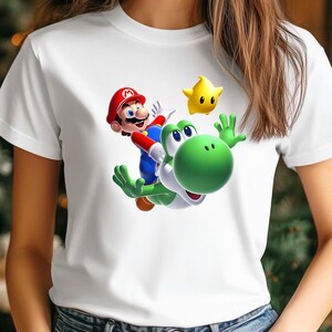 Op de afbeelding: Wit T-shirt met een kleurrijke afbeelding van Mario die op Yoshi rijdt, vergezeld van een gele ster. Het ontwerp is gecentreerd op het shirt. Het T-shirt is gemaakt van een zacht, comfortabel materiaal.
