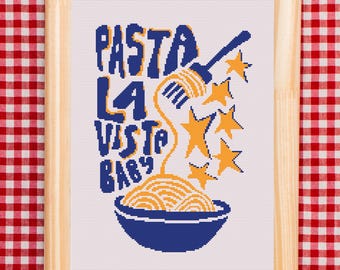 May include: A cross-stitch embroidery in a light wood frame featuring the text PASTA LA VISTA BABY in blue letters. A blue fork lifts yellow spaghetti from a blue bowl, surrounded by yellow stars on a white fabric background with a grid pattern.