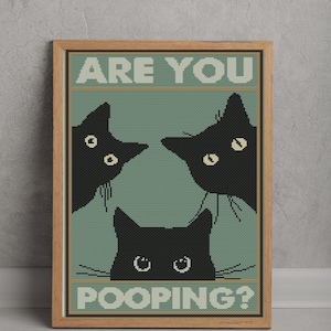 May include: A framed cross-stitch wall art piece featuring three black cats peering from the edges of a sage green background. The text ARE YOU is printed in white at the top, and the word POOPING? is printed in white at the bottom of the design.