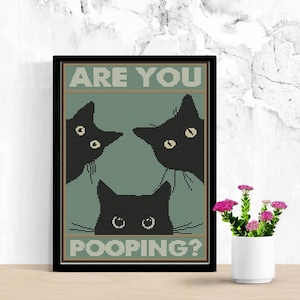 May include: A framed cross-stitch wall art piece featuring three black cat silhouettes against a muted sage green background. The text ARE YOU POOPING? is printed in white block letters at the top and bottom of the design within a dark border.