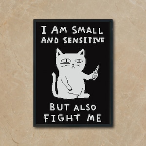 Puede incluir: Impresión artística enmarcada en negro con una ilustración de un gato blanco sosteniendo un cuchillo. El texto dice "I AM SMALL AND SENSITIVE BUT ALSO FIGHT ME". El gato tiene una expresión gruñona.