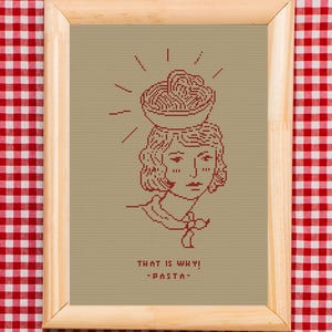 May include: Cross-stitch artwork in a wooden frame. The design shows a woman with a bowl of spaghetti on her head, with the text "THAT IS WHY! -PASTA-" in red. The background is tan, and the frame is on a red and white checkered tablecloth.