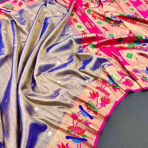 May include: A vibrant, draped textile with a shimmering blue and gold base. The fabric features a bright pink border adorned with floral and bird motifs in red, green, and blue. The overall design suggests a traditional garment.