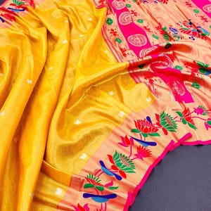 May include: A vibrant yellow saree with intricate floral and bird patterns in pink, green, and blue. The saree features a detailed border with lotus and bird motifs, and a contrasting peach-colored section with large pink circular designs.