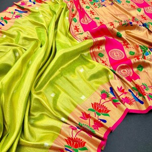 May include: A vibrant, draped saree in shades of chartreuse and gold. The saree features intricate floral and bird patterns along the borders, accented with bright pink and red details. The fabric has a lustrous sheen, suggesting a silk or satin material.