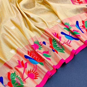 May include: A gold-colored sari with intricate floral and bird patterns. The border features a vibrant design with pink, red, blue, and green elements. The fabric has a subtle sheen, adding to its luxurious appearance.