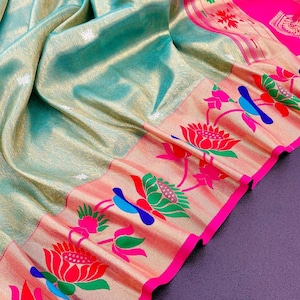 May include: A draped textile with a shimmering, light teal background. The border features a peach-colored design with floral and bird motifs in red, green, blue, and pink. A bright pink border frames the design.