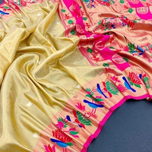 May include: A golden-yellow sari with intricate floral and bird patterns in pink, red, green, and blue. The sari features a vibrant pink border and a shimmering, textured appearance, showcasing traditional Indian textile design.