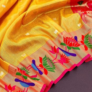 May include: A vibrant yellow saree with intricate floral and bird patterns. The border features red, pink, green, and blue designs on a gold background, with a bright pink trim. The fabric has a subtle sheen.