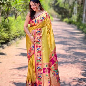 May include: A golden yellow sari with intricate floral and bird embroidery in shades of pink, blue, and green. The sari features a vibrant pink border and is draped elegantly. The overall design is rich and detailed, showcasing traditional Indian textile art.
