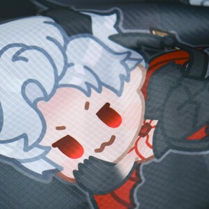May include: A white and red cartoon character with a black outline and red eyes. The character is wearing a red and black outfit. The background is a dark grey fabric.