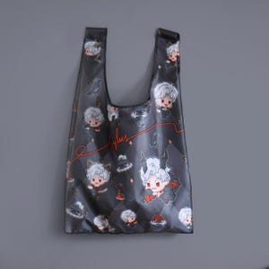 May include: A black reusable tote bag with a white and red cartoon character design. The bag features a repeating pattern of the character with different expressions and poses. The bag has a black handle and the text "Byulues" is printed on the front.