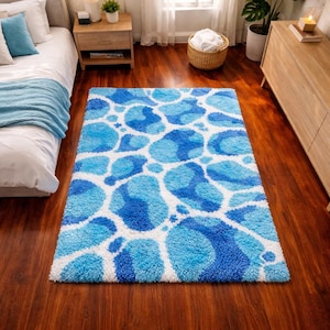 May include: A rectangular rug with a pattern of blue and white organic shapes. The rug has a shaggy texture and is placed on a dark wood floor. The color palette includes shades of blue and white, creating a modern and stylish look. The rug is a decorative element for a bedroom.