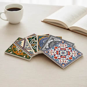 May include: A selection of square ceramic coasters with detailed patterns in various colours. The coasters display designs in green, blue, orange, and white. A white coffee cup and an open book are in the background.