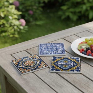 K&ouml;nnte beinhalten: Drei quadratische Keramikuntersetzer mit farbenfrohen Mustern. Einer zeigt ein florales Design mit orangefarbenen, gr&uuml;nen und blauen Akzenten. Ein weiterer hat ein blau-wei&szlig;es Muster, und der dritte sagt "LISBON".