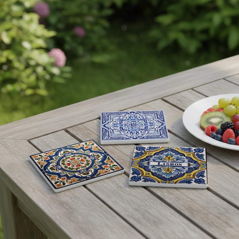 K&ouml;nnte beinhalten: Drei quadratische Keramikuntersetzer mit farbenfrohen Mustern. Einer zeigt ein florales Design mit orangefarbenen, gr&uuml;nen und blauen Akzenten. Ein weiterer hat ein blau-wei&szlig;es Muster, und der dritte sagt "LISBON".