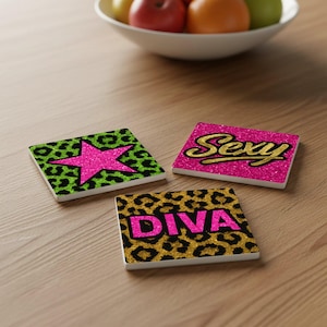 Könnte beinhalten: Drei quadratische Untersetzer mit Glitzerdesigns. Einer hat einen pinkfarbenen Stern auf einem grünen Leopardenmuster-Hintergrund. Ein anderer Schriftzug "Sexy" in goldener Schrift auf pinkfarbenem Hintergrund. Der dritte Schriftzug "DIVA" in Pink auf goldenem Leopardenmuster.