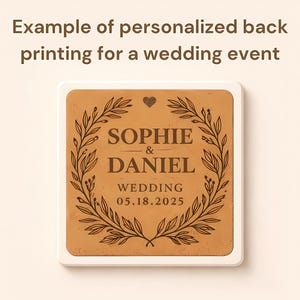 K&ouml;nnte beinhalten: Quadratischer, hellbrauner Hochzeitsanh&auml;nger mit wei&szlig;em Rand. In der Mitte stehen die Namen "Sophie & Daniel" und das Hochzeitsdatum "05.18.2025" in einem dekorativen Blumenkranz. Der Text "Example of personalized back printing for a wedding event" steht oben.