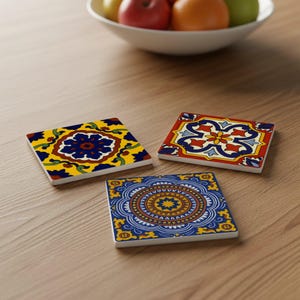 May include: Three square ceramic coasters with vibrant, detailed patterns. One coaster displays a blue floral design on a yellow base. Another has a red and blue floral pattern. The third coaster features a blue and gold circular design.