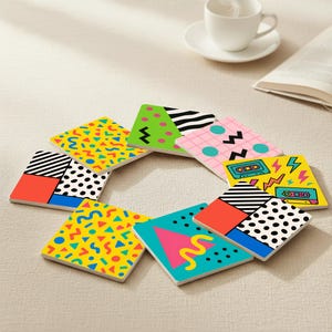 Op de afbeelding: Een verzameling vierkante onderzetters met levendige ontwerpen geïnspireerd op de jaren 80. Elke onderzetter heeft een uniek patroon, waaronder geometrische vormen, zigzags, stippen en cassetteband graphics. De onderzetters zijn in een cirkel gerangschikt.