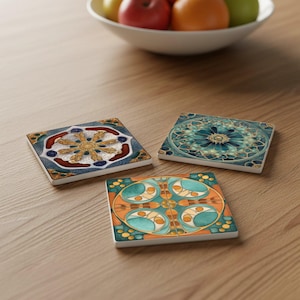 Può includere: Tre sottobicchieri quadrati in ceramica con disegni colorati e intricati. Uno presenta un motivo floreale oro e bianco su sfondo blu. Un altro ha un design floreale turchese e oro. Il terzo sottobicchiere ha un motivo geometrico arancione e turchese.