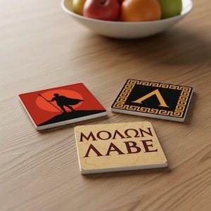 May include: A set of three square ceramic coasters. One coaster features a silhouette of a figure with a spear against a red sun. Another has a black background with a gold lambda symbol. The third coaster has the text "MOLON LABE".