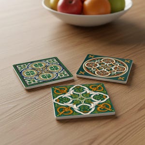 Puede incluir: Tres posavasos cuadrados de cerámica con intrincados diseños de nudos celtas en verde, dorado y blanco. Un posavasos presenta un patrón de trébol de cuatro hojas. Los posavasos están sobre una superficie de madera.