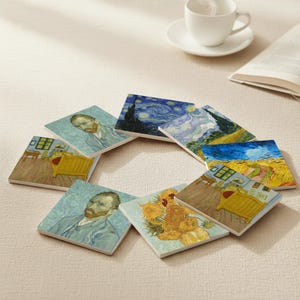 Op de afbeelding: Een set vierkante keramische onderzetters met beroemde schilderijen van Vincent van Gogh. De onderzetters tonen afbeeldingen van zonnebloemen, zelfportretten en landschappen, waaronder "Starry Night". Een witte theekop en een boek staan op de achtergrond.
