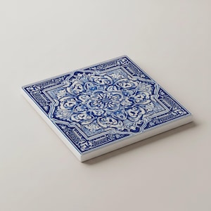 K&ouml;nnte beinhalten: Quadratische Keramikfliese mit blau-wei&szlig;em Blumenmuster. Das Design zeigt ein zentrales Blumenmotiv, umgeben von aufwendigen Schn&ouml;rkeln und einem Rand. Die Fliese ist vor einem wei&szlig;en Hintergrund platziert.