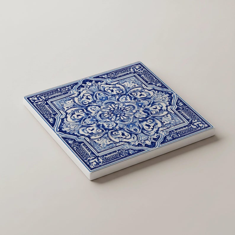 K&ouml;nnte beinhalten: Quadratische Keramikfliese mit blau-wei&szlig;em Blumenmuster. Das Design zeigt ein zentrales Blumenmotiv, umgeben von aufwendigen Schn&ouml;rkeln und einem Rand. Die Fliese ist vor einem wei&szlig;en Hintergrund platziert.